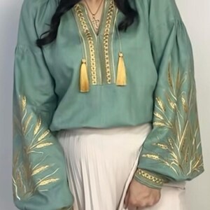 May include: A sage green linen blouse with gold embroidery of wheat stalks on the sleeves and a gold chain design with tassels on the neckline.