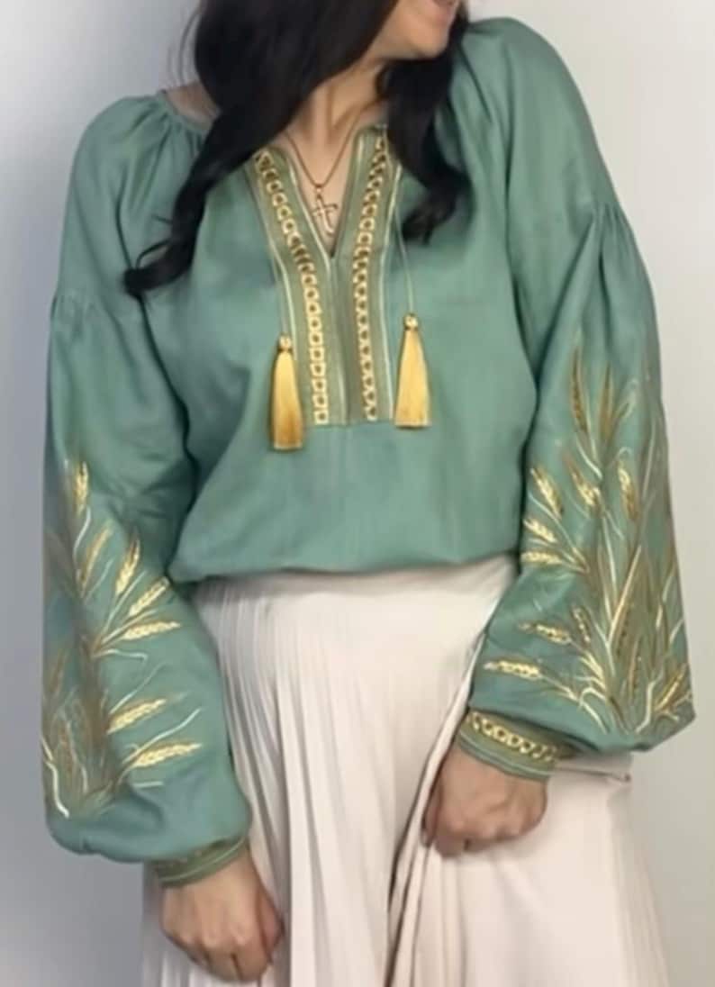 May include: A sage green linen blouse with gold embroidery of wheat stalks on the sleeves and a gold chain design with tassels on the neckline.