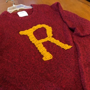 May include: A maroon sweater with a large yellow embroidered letter "R" on the front.