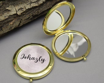 Peut inclure: Un miroir de poche doré avec un fond blanc et le nom "Johazly" imprimé en lettres cursives noires.