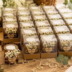 Pu&ograve; includere: Una collezione di piccoli portacandele in legno con lumini bianchi, ciascuno racchiuso in una scatola quadrata trasparente. Ogni portacandele &egrave; decorato con fiori bianchi di gipsofila e un'etichetta in legno a forma di cuore.