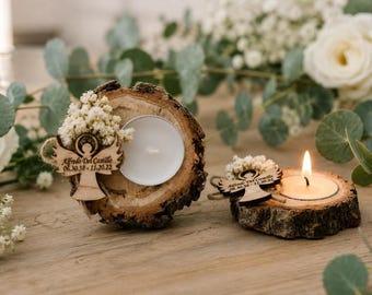 May include: Two natural wood slice candle holders featuring a small white tea light candle and a wooden angel cutout. The angel is engraved with the text Alfredo Del Castillo 06.30.38 - 11.20.22 and adorned with small white dried flowers.