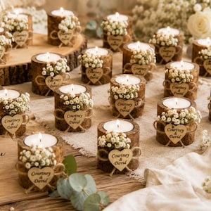Pu&ograve; includere: Una collezione di portacandele cilindrici in legno, ognuno con un lumino bianco, piccoli fiori bianchi e un'etichetta in legno a forma di cuore incisa con il testo Courtney & David. Un cartello in legno riporta thank you for celebrating with us.