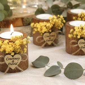 Pu&ograve; includere: Tre portacandele cilindrici in legno con lumini, decorati con fiori gialli e una piccola etichetta in legno a forma di cuore legata con dello spago. Ogni cuore reca l'incisione del testo Courtney & David su un tessuto chiaro.
