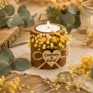 Pu&ograve; includere: Un portacandele cilindrico in legno con un lumino acceso, decorato con fiori secchi gialli e una piccola targhetta in legno a forma di cuore legata con dello spago. Il cuore reca l'incisione Courtney & David in inchiostro nero.
