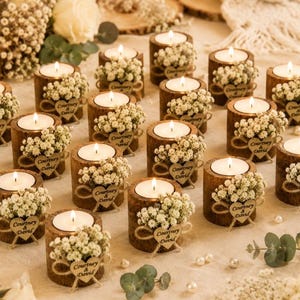 Pu&ograve; includere: Una collezione di portacandele cilindrici in legno, ciascuno contenente un lumino bianco. I supporti sono decorati con fiori bianchi di gipsofila e una piccola targhetta in legno a forma di cuore con inciso il testo Courtney & David.