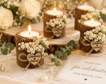 Puede incluir: Tres portavelas cilíndricos de madera con corteza exterior, cada uno con una vela de té encendida. Cada portavelas está decorado con flores blancas de paniculata y una pequeña etiqueta de madera en forma de corazón grabada con Courtney & David.