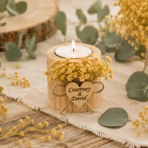 Pu&ograve; includere: Un portacandele cilindrico in legno con un lumino bianco acceso. Il supporto &egrave; decorato con fiori secchi gialli e una piccola targhetta in legno a forma di cuore legata con dello spago, incisa con il testo Courtney & David.