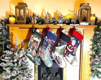 Pode incluir: Quatro meias de Natal com designs festivos penduradas acima de uma lareira. As meias apresentam cenas do Papai Noel, renas e paisagens de inverno. A lareira é decorada com vegetação, velas e lanternas decorativas, criando uma atmosfera acolhedora.