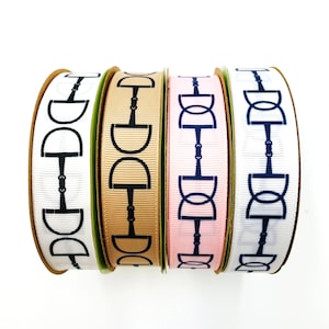 May include: Four spools of ribbon with a black equestrian bit design. The ribbons are white, beige, pink, and white.