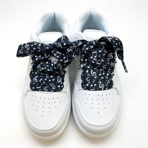 May include: White sneakers with black and white musical note patterned shoelaces tied in a bow.
