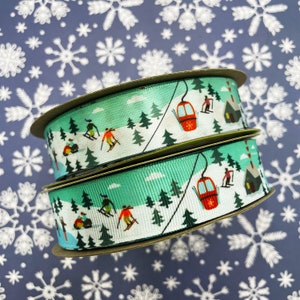 May include: Two rolls of green and white ribbon with a winter sports theme. The ribbon features skiers, a ski lift, and a small cabin.