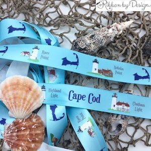May include: Blue satin ribbon with a repeating pattern of lighthouses and the text "Cape Cod" and the names of different lighthouses on Cape Cod, including Race Point, Nobska Point, Highland Light, and Chatham Light.