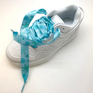 May include: White sneakers with blue snowflake patterned shoelaces. The laces are tied in a bow.