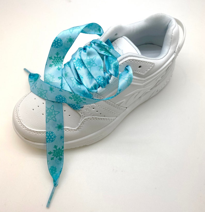 May include: White sneakers with blue snowflake patterned shoelaces. The laces are tied in a bow.