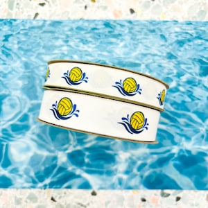 May include: Two rolls of white ribbon with a repeating pattern of yellow water polo balls with blue water splashes.