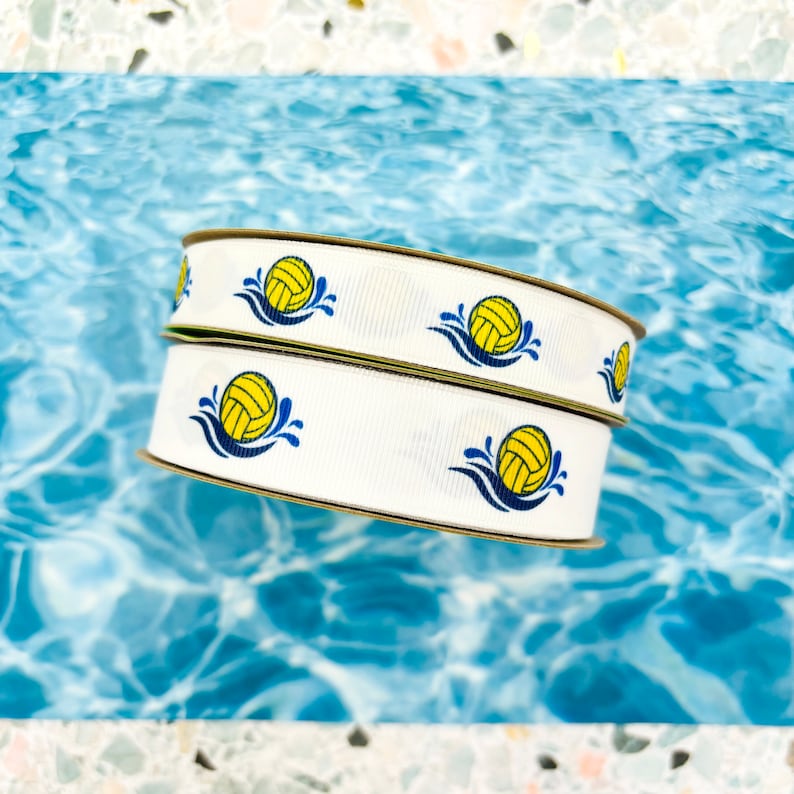 May include: Two rolls of white ribbon with a repeating pattern of yellow water polo balls with blue water splashes.