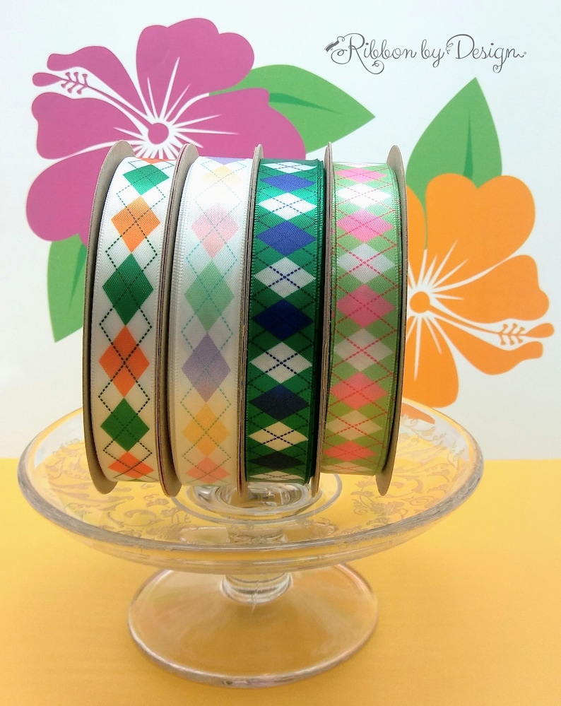 Puede incluir: Cuatro carretes de cinta con un patr&oacute;n de diamante. Las cintas son verde, rosa, azul y amarilla con diamantes blancos. Las cintas est&aacute;n sobre un pedestal de vidrio sobre un fondo amarillo.