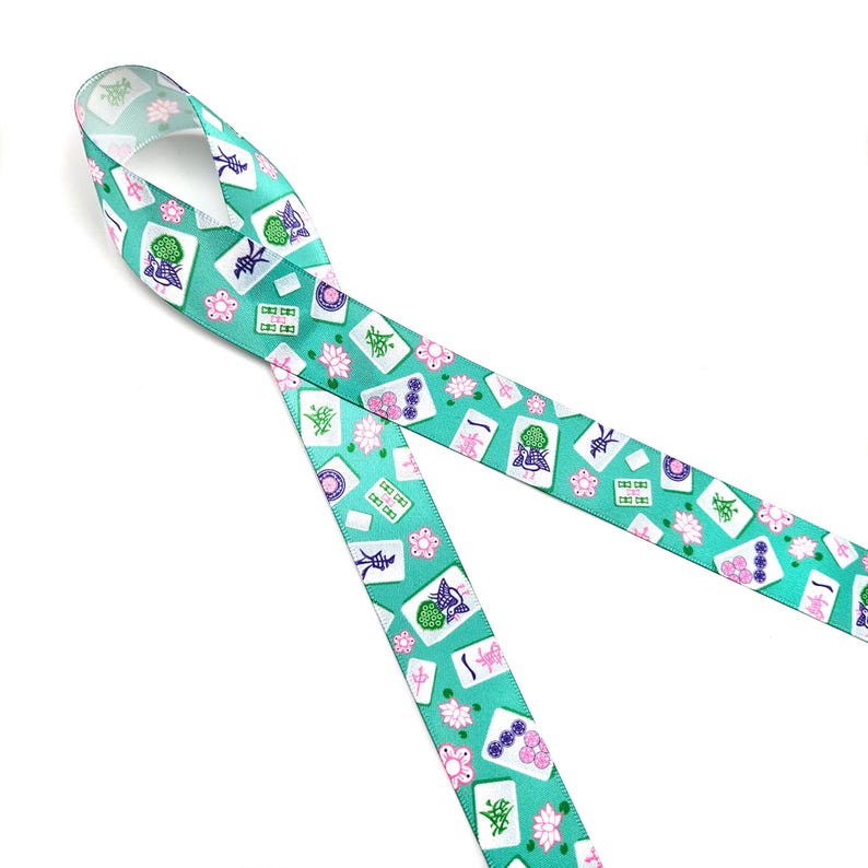 May include: A teal ribbon featuring a repeating pattern of Mahjong tiles, pink flowers, and other symbols. The ribbon is made of a smooth material and is ideal for crafting or gift wrapping. The design includes various colors, including white, green, pink, and purple.