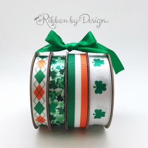 May include: Four rolls of green, white, and orange patterned ribbon with shamrock designs. The ribbon is tied with a green bow and the text "Ribbon by Design" is visible in the background.