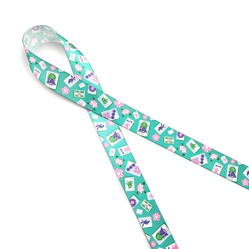 May include: A teal ribbon with a repeating pattern of Mahjong tiles, flowers, and other symbols. The ribbon is made of a smooth material and is ideal for crafting or gift wrapping.