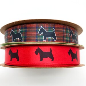 May include: Two spools of ribbon. The top spool features a plaid pattern in shades of brown, green, and blue, with black dog silhouettes. The bottom spool is red with black dog silhouettes. Both spools are on cardboard.
