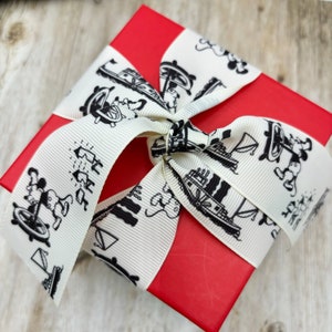 K&ouml;nnte beinhalten: Eine rote Geschenkbox mit einem wei&szlig;en Band. Das Band ist mit schwarz-wei&szlig;en Illustrationen von Mickey Mouse und Booten verziert.