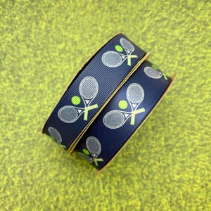 May include: Two spools of navy blue ribbon with a white tennis racket and green tennis ball design.