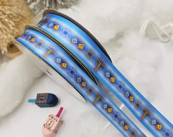 Könnte beinhalten: Blaue Bandspulen mit einem sich wiederholenden Muster aus Menora, Dreideln und Davidsternen. Zwei kleine Dreidel befinden sich im Vordergrund. Das Band ist eine festliche Dekoration für Chanukka oder andere jüdische Feiern.