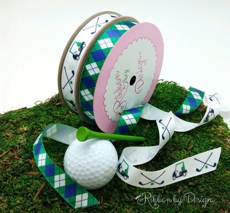 Puede incluir: Dos carretes de cinta con tem&aacute;tica de golf. Un carrete tiene un fondo blanco con carritos de golf verdes y palos de golf impresos en &eacute;l. El otro carrete tiene un patr&oacute;n de cuadros verdes y azules. Tambi&eacute;n hay una pelota de golf y un tee de golf verde en la imagen. El texto en el carrete dice "Ribbon by Design."