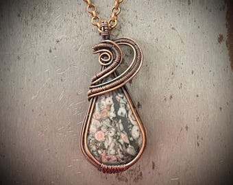 May include: A copper wire wrapped pendant featuring a teardrop-shaped stone with a gray, black, and pink speckled pattern.