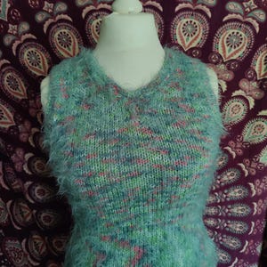 Könnte beinhalten: Ein flauschiger, blaugrüner ärmelloser Pullover mit V-Ausschnitt. Der Pullover ist aus mehrfarbigem Garn mit rosa, grünen und weißen Akzenten.