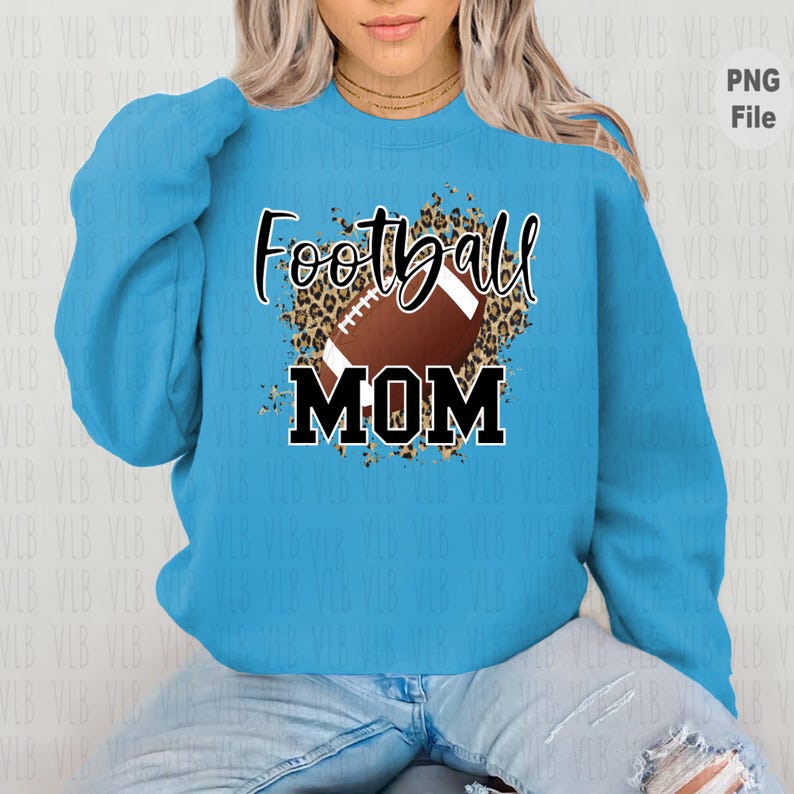 May include: A light blue sweatshirt with a graphic design of a football with a leopard print background. The text "Football Mom" is printed in black letters.
