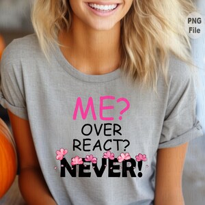 Pode incluir: Uma camiseta cinza com o texto "ME? OVER REACT? NEVER!" em rosa e preto. Gráficos de flores rosa estão abaixo do texto. A camisa tem mangas enroladas.