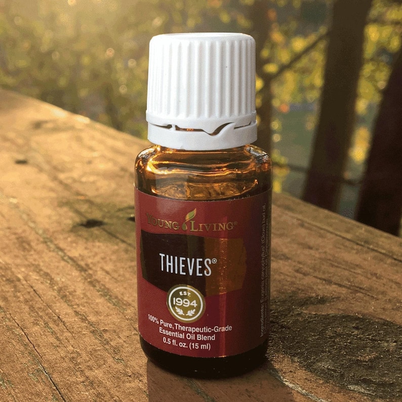 May include: A small amber glass bottle of Young Living Thieves essential oil. The bottle has a white cap and a maroon label with the text "THIEVES" and "1994". The bottle contains 0.5 fl. oz. (15 ml) of 100% pure, therapeutic-grade essential oil.