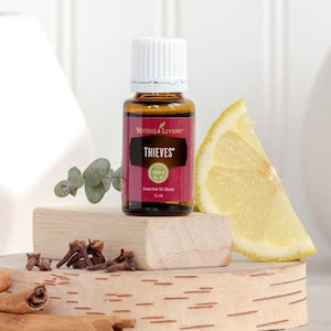May include: A 15 ml bottle of Young Living Thieves essential oil blend with a white cap and a red label. The image includes a lemon wedge, cloves, and eucalyptus sprigs on a wooden block.