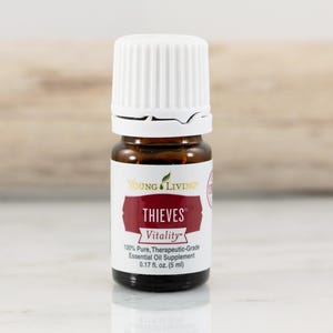 May include: A small brown glass bottle with a white cap. The label reads "THIEVES Vitality" and "100% Pure, Therapeutic-Grade Essential Oil Supplement 0.17 fl. oz. (5 ml)". The bottle is for essential oils.