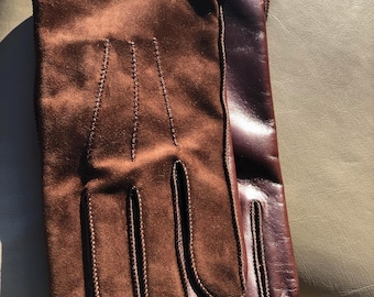 May include: A pair of gloves featuring a brown suede top side with decorative stitching on the back of the hand and a smooth dark brown leather underside. The gloves have a clean finish with visible seams along the fingers and a small red stitch detail.