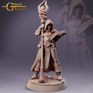 May include: A detailed miniature figure of a robed mage holding a staff and a book. The figure is in a standing pose, with a hood and intricate detailing on the clothing and accessories. The base is a circular platform. The figure is a light tan color.