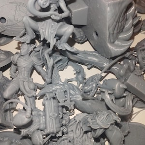 May include: A collection of unpainted gray miniature figurines, including fantasy characters and creatures. The figures are in various poses and sizes, suggesting a tabletop gaming or hobbyist theme.