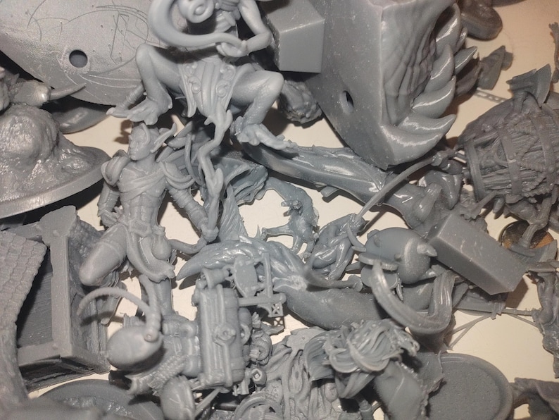 May include: A collection of unpainted gray miniature figurines, including fantasy characters and creatures. The figures are in various poses and sizes, suggesting a tabletop gaming or hobbyist theme.