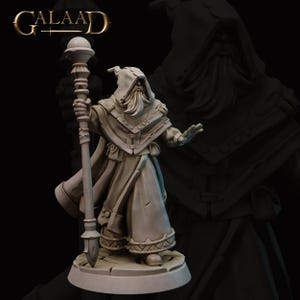 May include: A detailed figurine of a robed wizard with a long beard and hooded cloak, holding a staff with a spherical top. The figure is standing on a stone base. The word "GALAAD" is in the upper left corner.