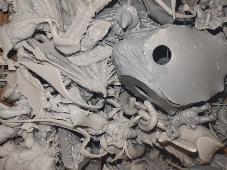 May include: A pile of unassembled, light gray plastic model kit parts. The components include dragon wings, figures, and architectural elements. The parts are intricately detailed and appear to be from a fantasy or sci-fi themed model kit.