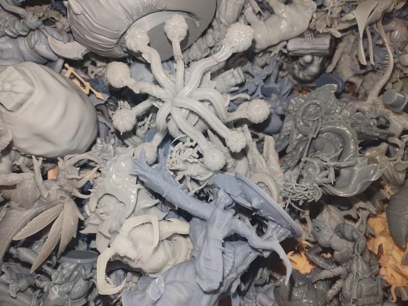 May include: A collection of unpainted, gray miniature figurines. The assortment includes fantasy creatures, such as dragons, insects, and other otherworldly beings. Some figures have intricate details, while others are more abstract.