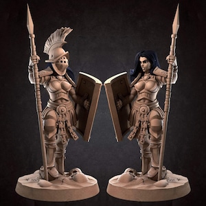 May include: Two statues of female gladiators, each holding a spear and shield. They wear detailed armor and helmets. The statues are on a sandy base, with a dark background.