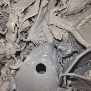 May include: A collection of unpainted, gray plastic miniatures, including dragons, fantasy creatures, and architectural elements. The pieces are intricately detailed, with visible wings, horns, and scales. The image suggests a hobby or model-making theme.