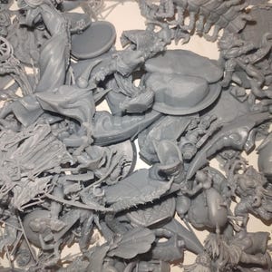 May include: A pile of unassembled gray plastic miniatures, likely for tabletop gaming. The components include figures, shields, and other detailed parts. The pieces are in various shapes and sizes, suggesting a fantasy or historical theme.