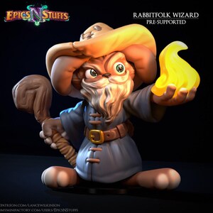 May include: A Rabbitfolk Wizard figurine, holding a staff and a glowing yellow orb. The wizard is dressed in a blue robe, a brown belt, and a tan hat. The text "Epics N' Stuffs" and "Rabbitfolk Wizard Pre-Supported" are visible.