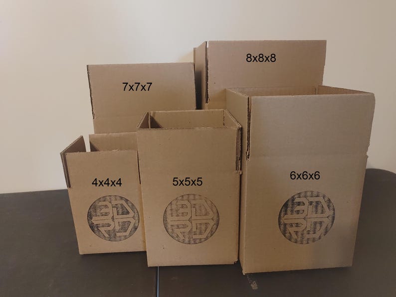 May include: A collection of brown cardboard boxes of varying sizes, labeled with dimensions such as 4x4x4 inches, 5x5x5 inches, 6x6x6 inches, 7x7x7 inches, and 8x8x8 inches. Each box features a circular logo. The boxes are arranged on a dark surface.