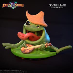 May include: A green Frogfolk Bard figurine with an orange hat and a red tongue sticking out. The frog is holding a small lute and sitting on a green lily pad. The text "Epics N Stuffs" and "FROGFOLK BARD PRE-SUPPORTED" are visible.